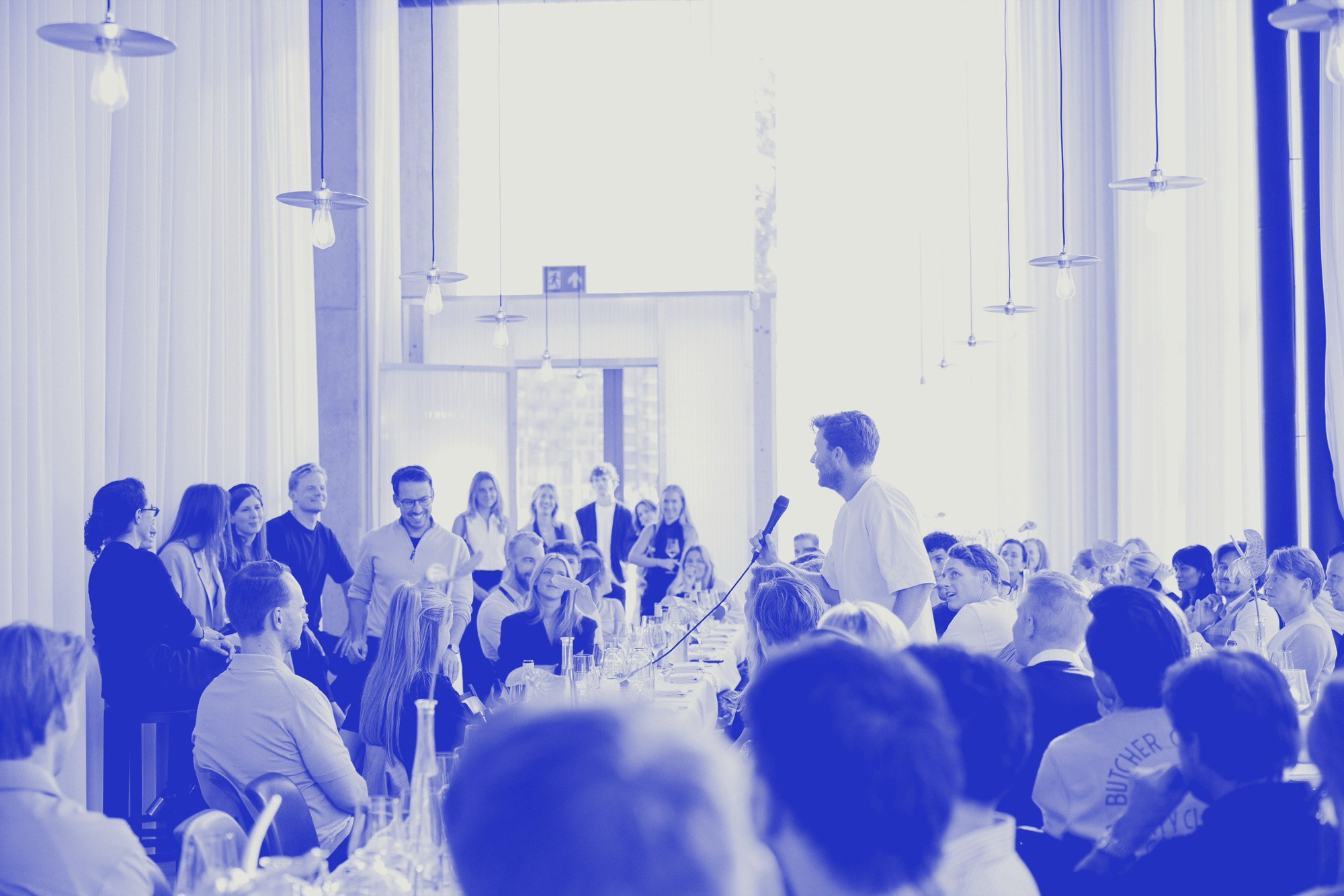 A long dinner table of founders, in ultramarine duotone